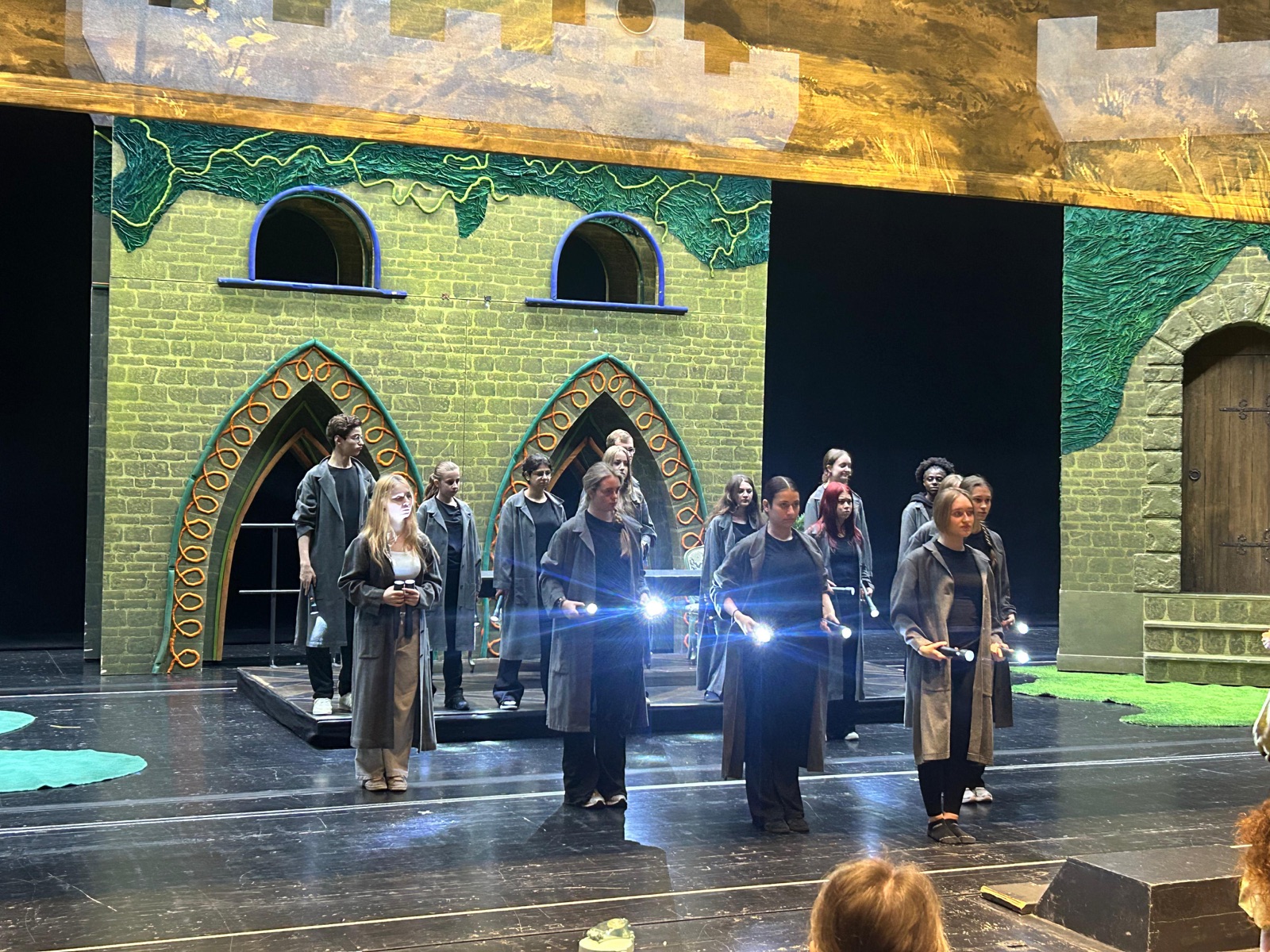 Schülerinnen und Schüler in Kostümen mit Taschenlampen auf der beleuchteten Bühne des Aalto-Theaters, im Hintergrund eine märchenhafte Burgkulisse