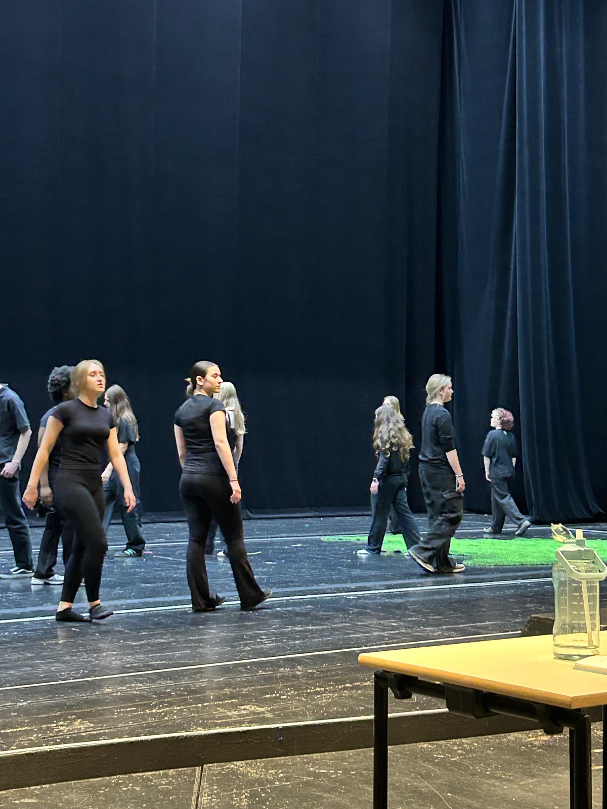 Schülerinnen und Schüler in schwarzer Probenkleidung gehen während einer Choreografie über die Bühne