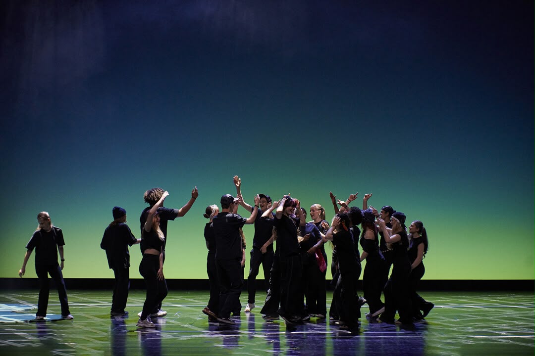Jubelndes Ensemble mit erhobenen Armen vor grün-blauem Bühnenlicht im Aalto-Theater