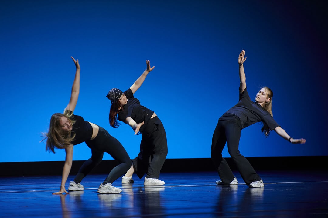 Drei Tänzerinnen in dynamischer Hip-Hop-Pose vor blauem Bühnenhintergrund