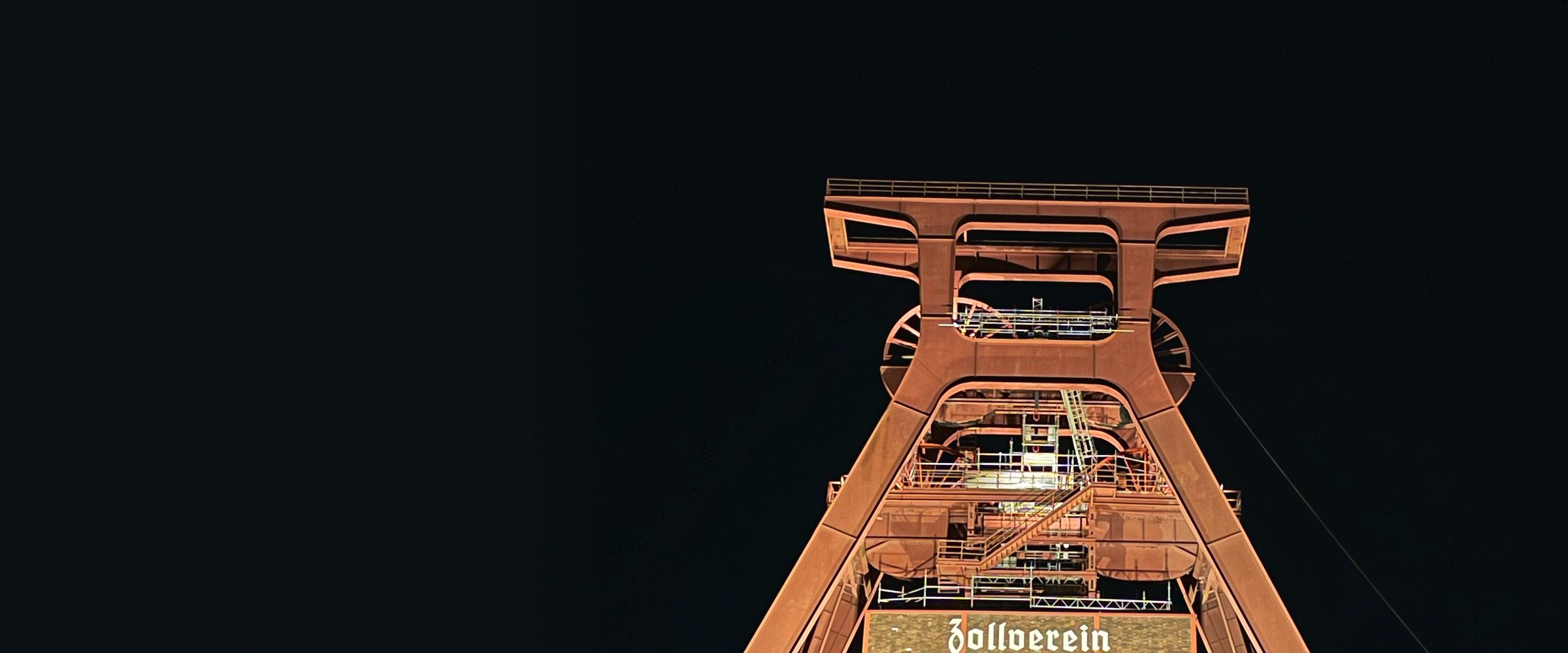 Beleuchteter Doppelbock-Förderturm der Zeche Zollverein bei Nacht